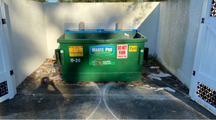 Dirty, stained dumpster pad inside an enclosure before cleaning