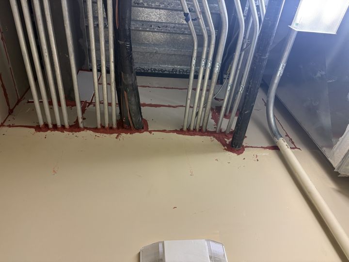 Red firestop sealant around conduit and pipe penetrations at a wall and ceiling