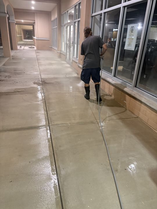 Crew member pressure washing a covered storefront walkway at night